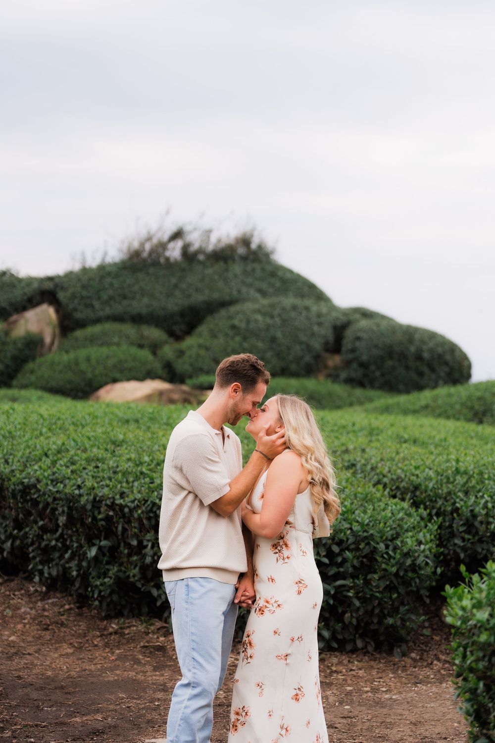 Romantic couple sharing a tender moment in a green tea garden during an outdoor engagement photo session.