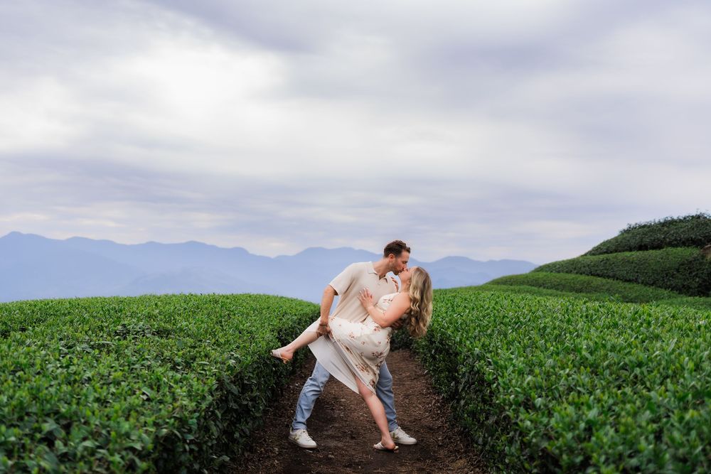Romantic couple sharing a dip kiss on a dirt path through a scenic green tea plantation.