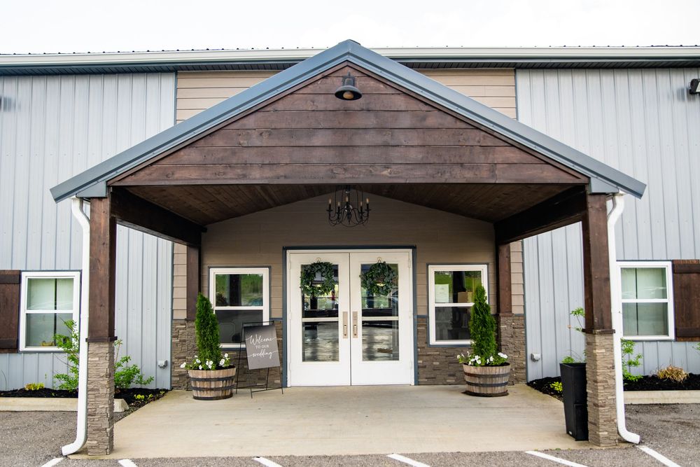 Elegant rustic wedding venue exterior with wood accents, double doors, and barrel planters.