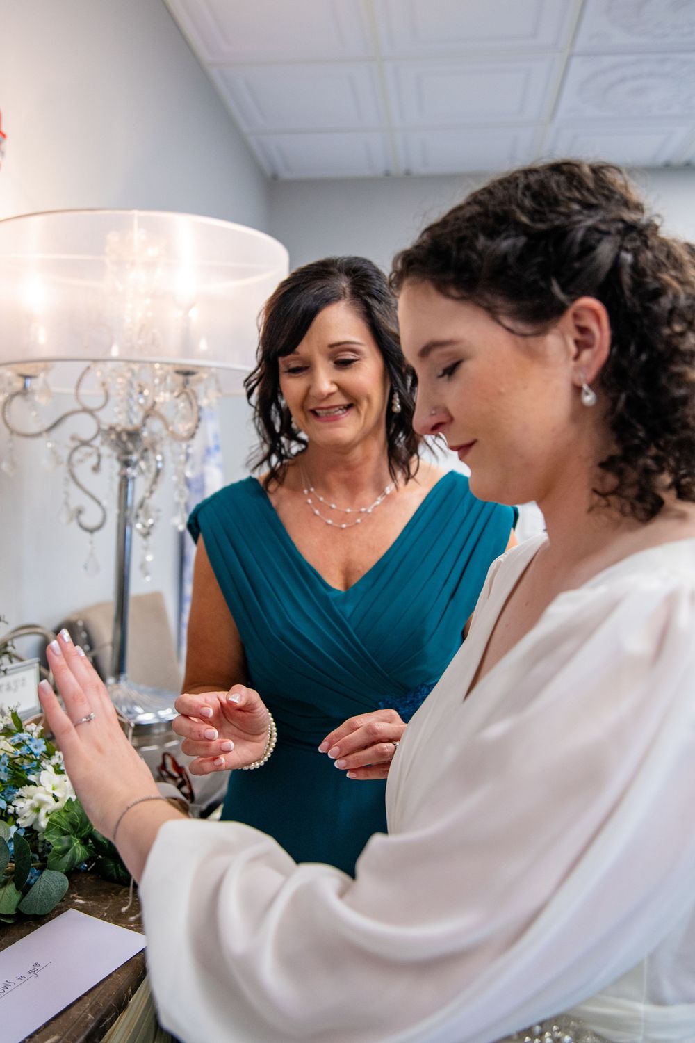 Bride and mother share a tender moment examining pearl jewelry during wedding preparations indoors.
