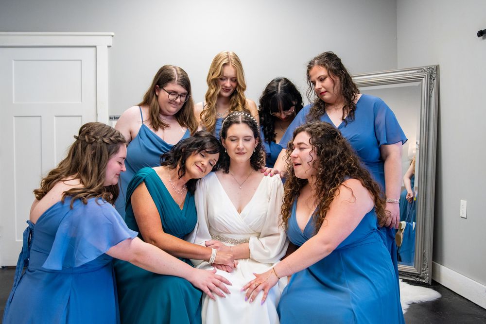 Bride surrounded by bridesmaids in blue dresses sharing a tender moment before the wedding ceremony.