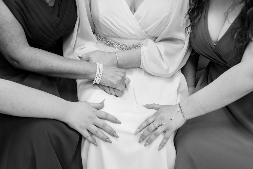 Black and white photo of hands resting on bride's lap during wedding day preparations.