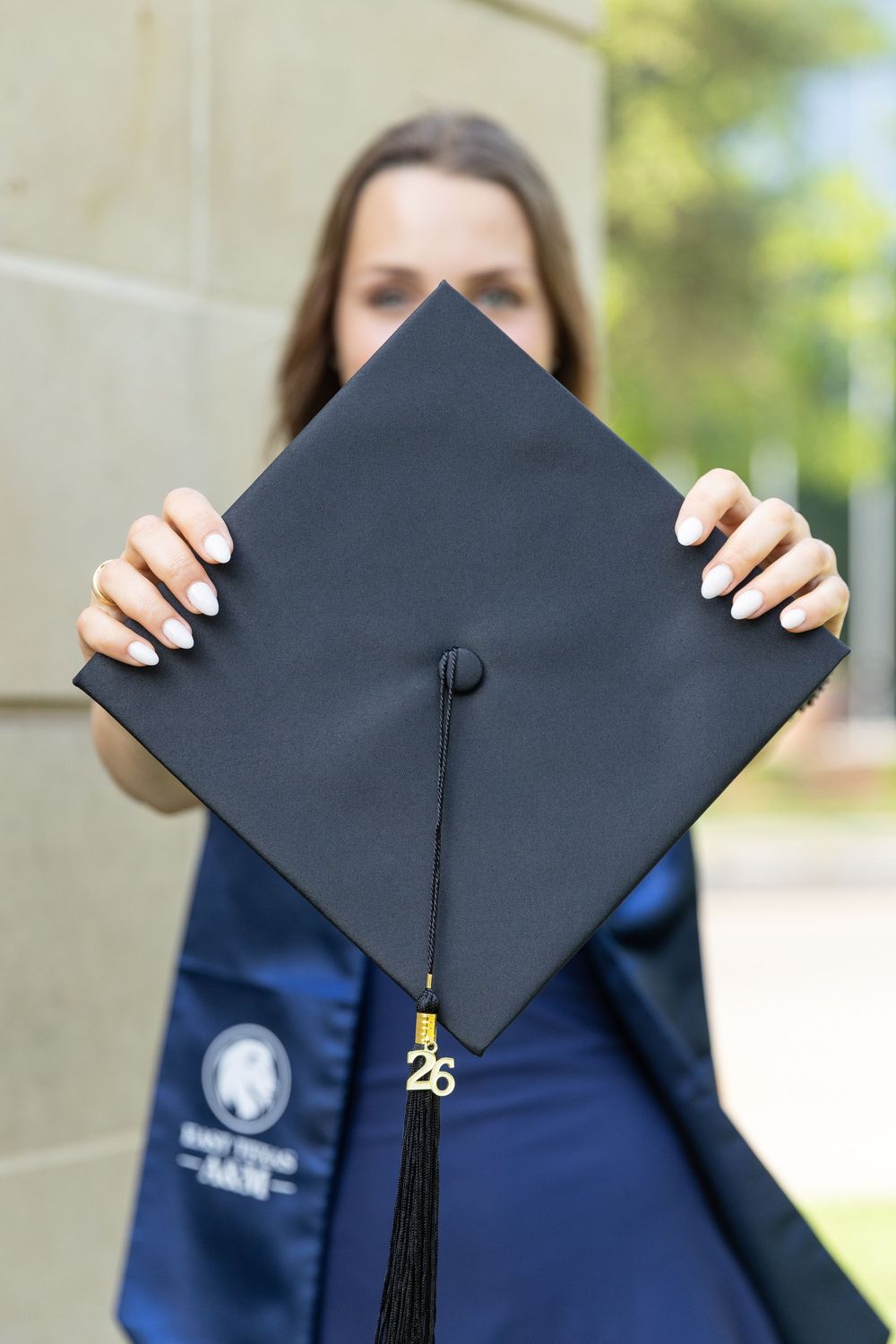 girl holding out cap and tassel with her out of focus in the background