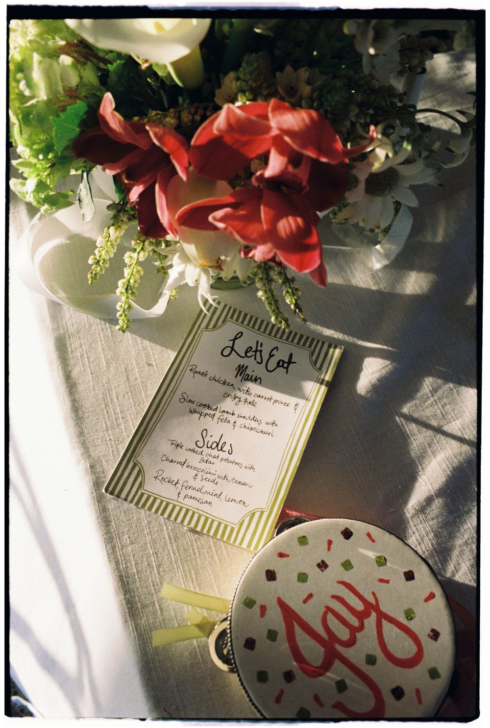 Elegant wedding table setting with red floral bouquet, handwritten menu card reading Let's Eat, and decorative round box.
