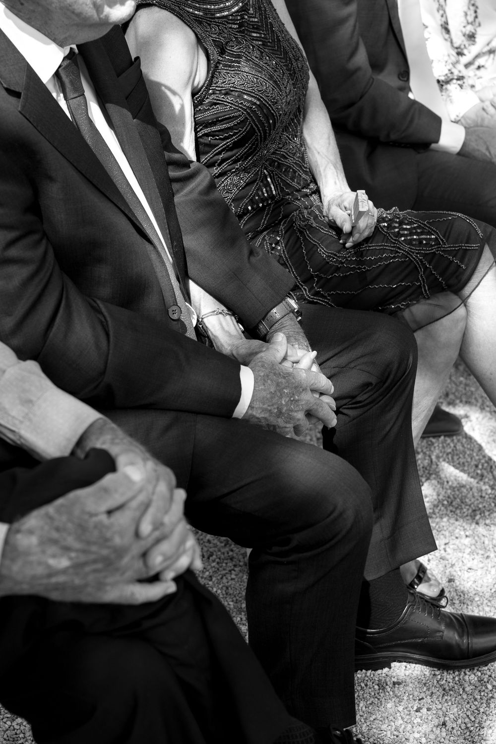 Black and white photo of elegantly dressed guests seated at a formal event, wearing suits and beaded dresses.