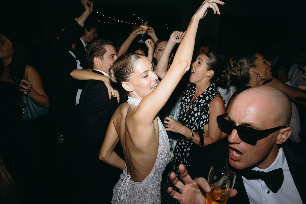 Guests dancing joyfully at an elegant wedding reception, woman in backless dress with arms raised.