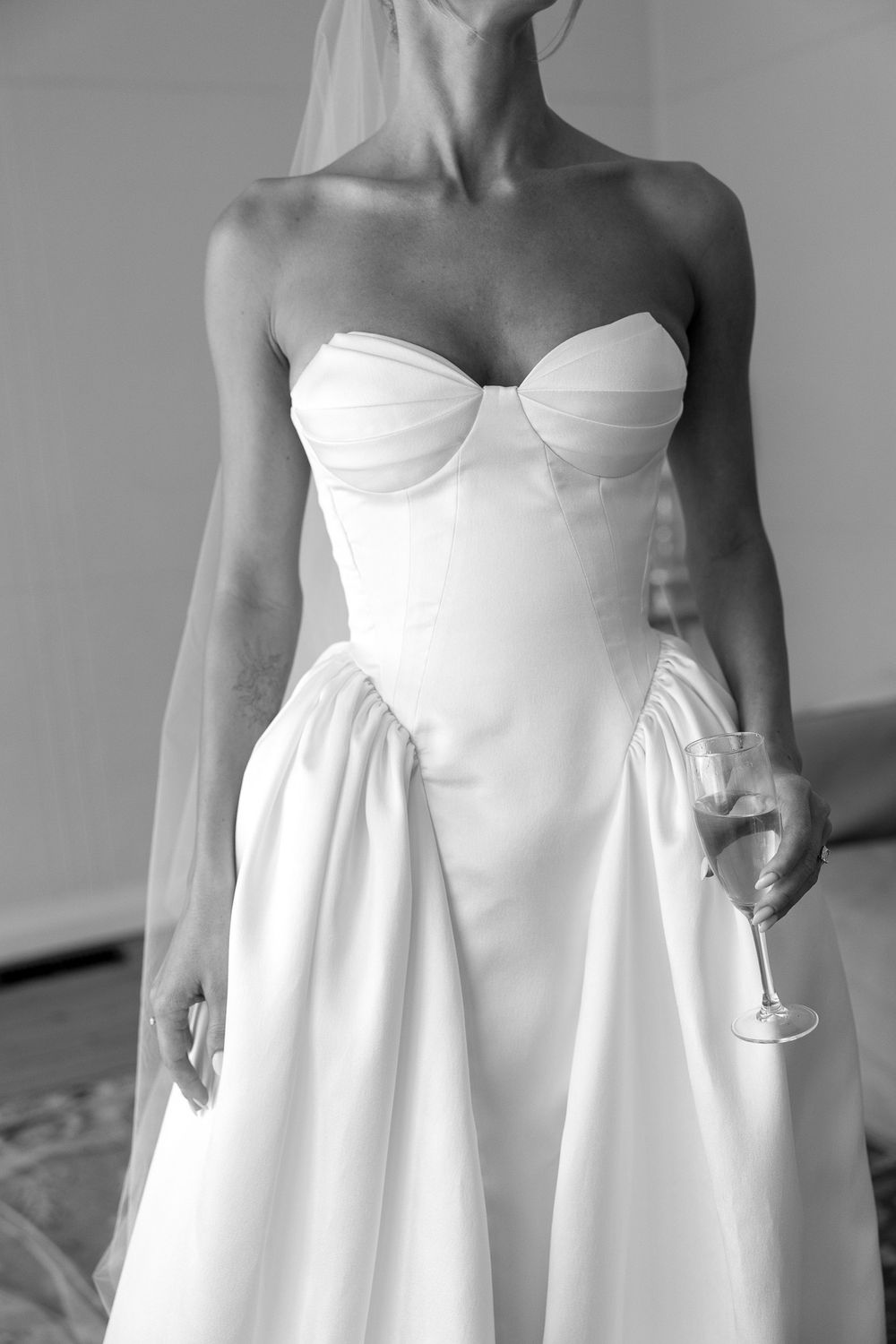 Black and white photo of a bride in a strapless white wedding gown holding a champagne glass.