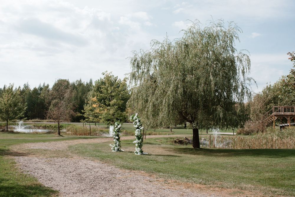 Outdoor wedding ceremony arch with floral decorations beside a willow tree in a scenic park setting.