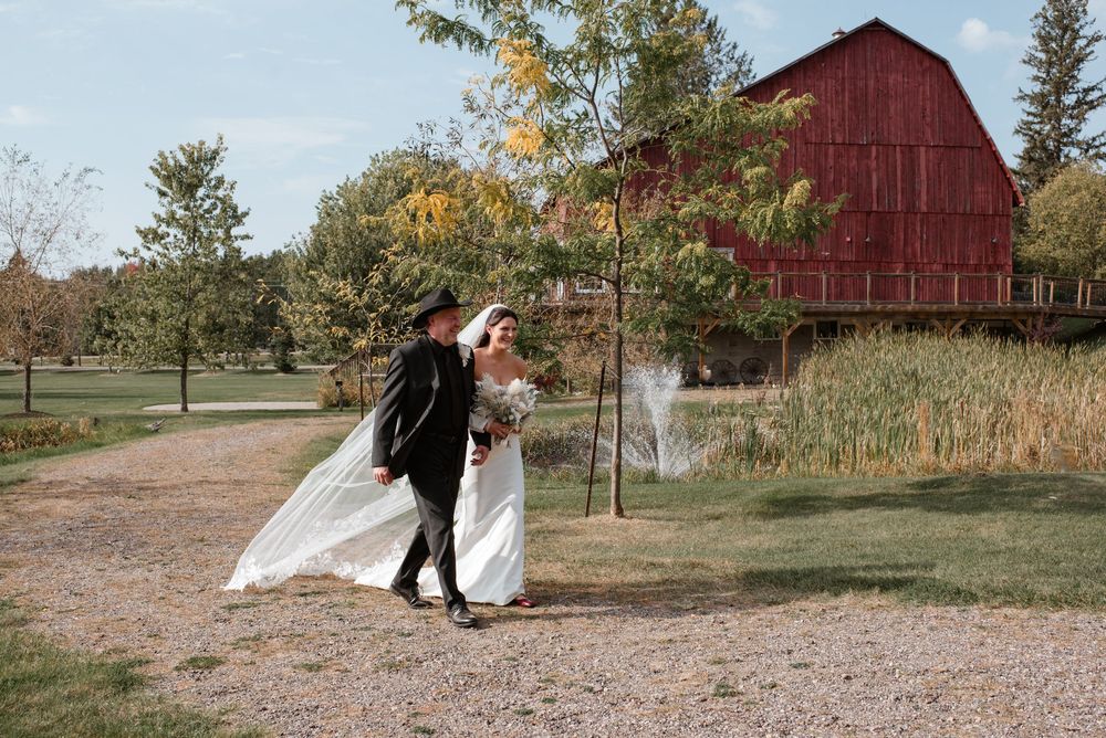 Bride and groom walk hand-in-hand near a red barn on a scenic fall wedding venue.