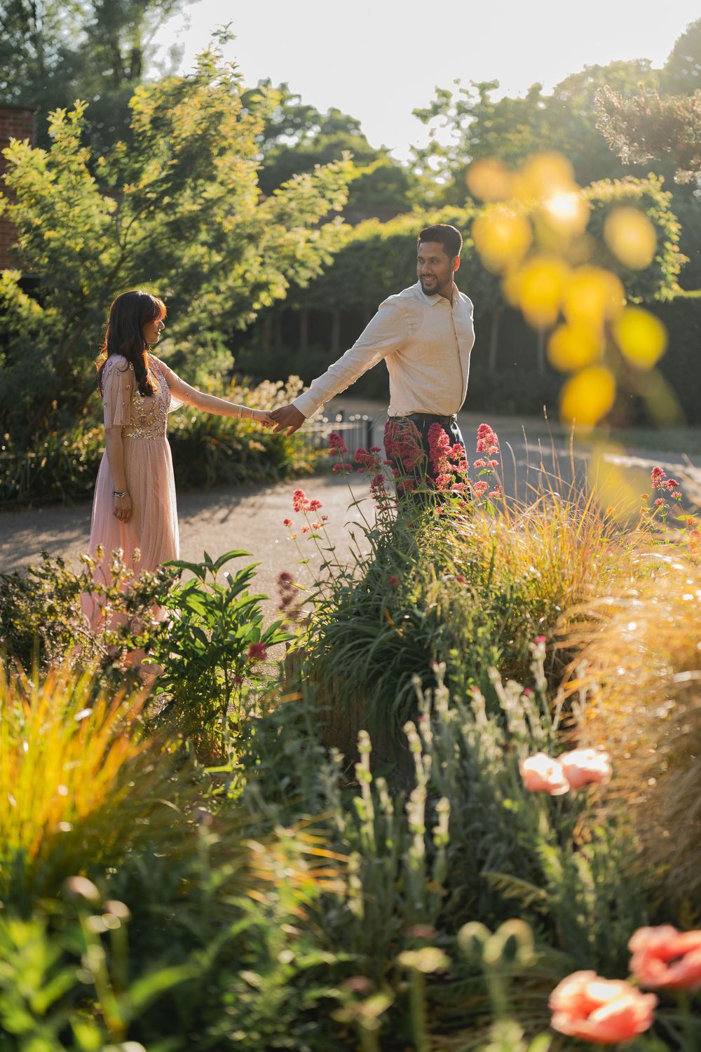 Couple holding hands in a sunlit garden surrounded by colorful wildflowers and lush greenery on a warm summer day.