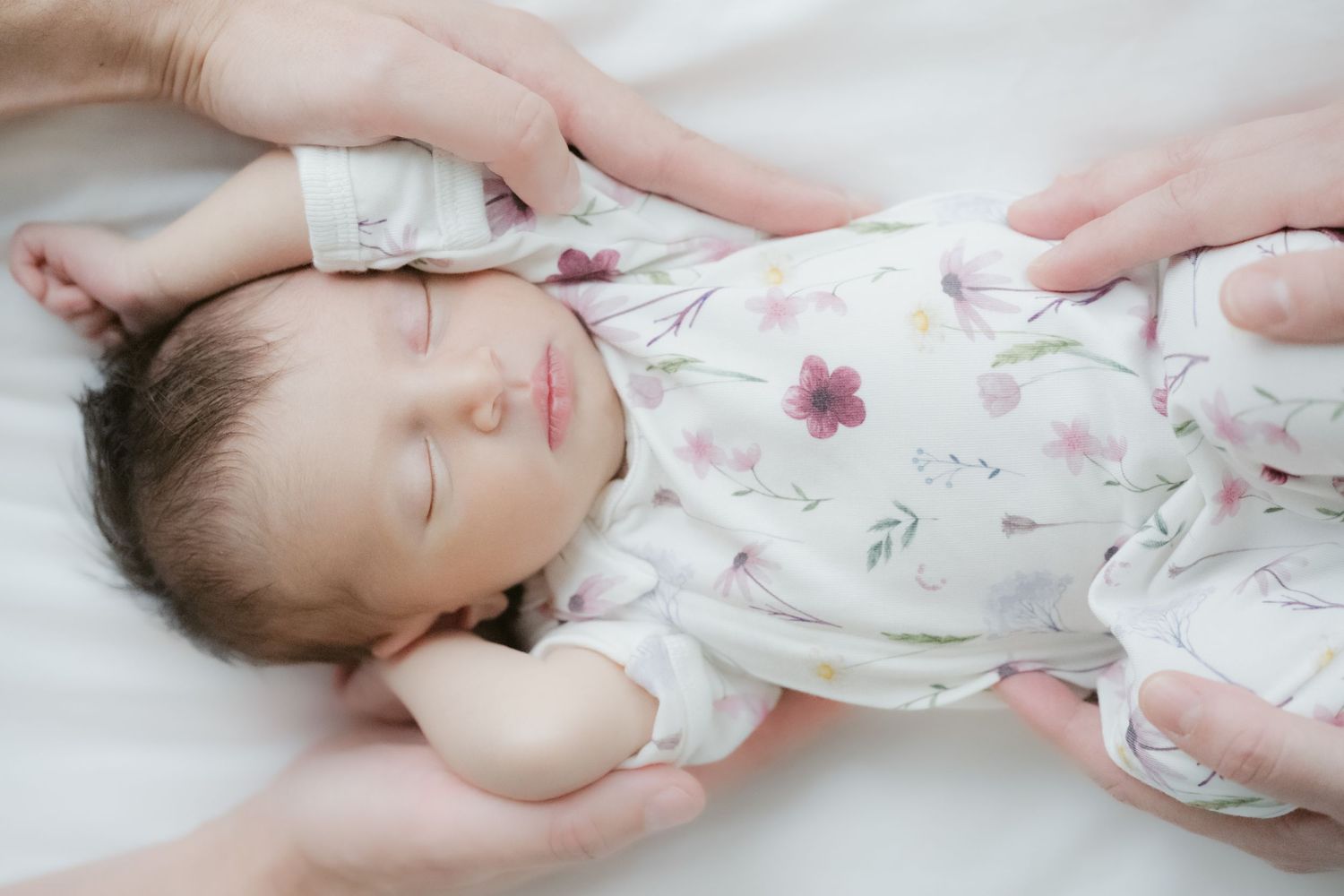 Sleeping newborn baby in floral onesie cradled by parent hands, newborn photography North Vancouver