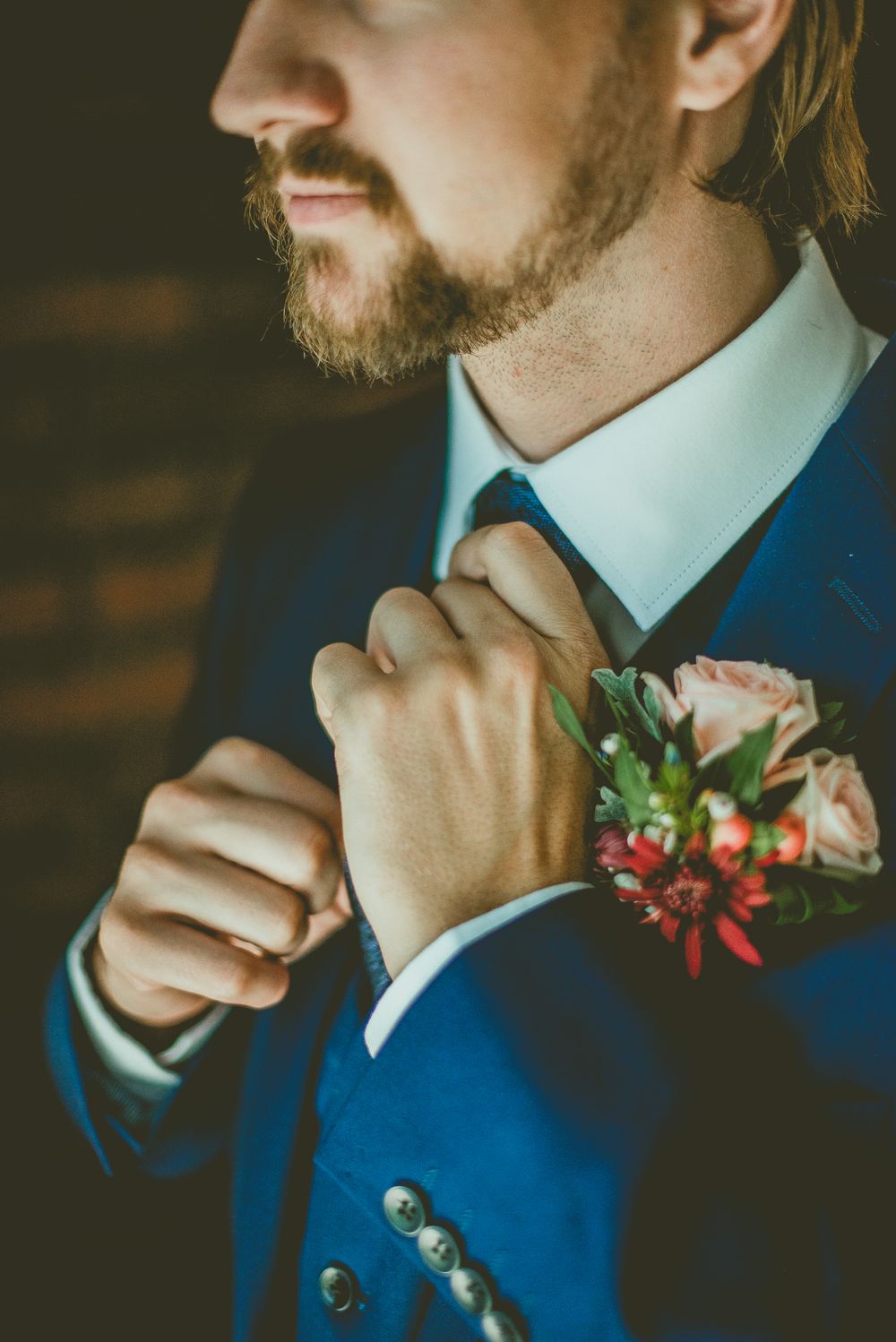 Groom in navy blue suit adjusting tie with floral boutonniere featuring pink roses on micro wedding day.