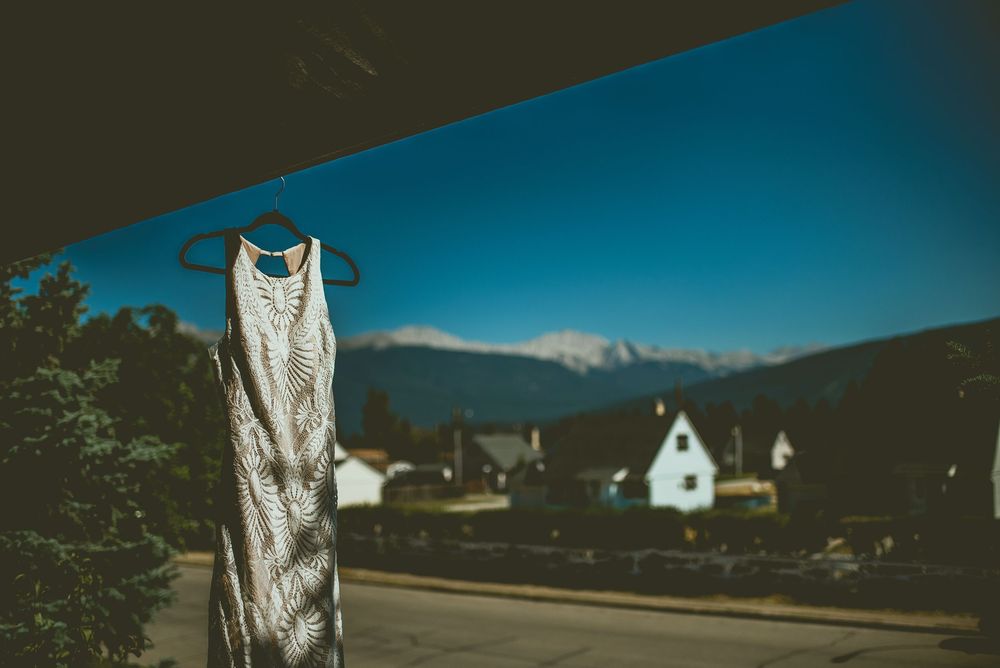 Elegant lace micro wedding dress hanging on hanger outdoors with mountain and blue sky backdrop.