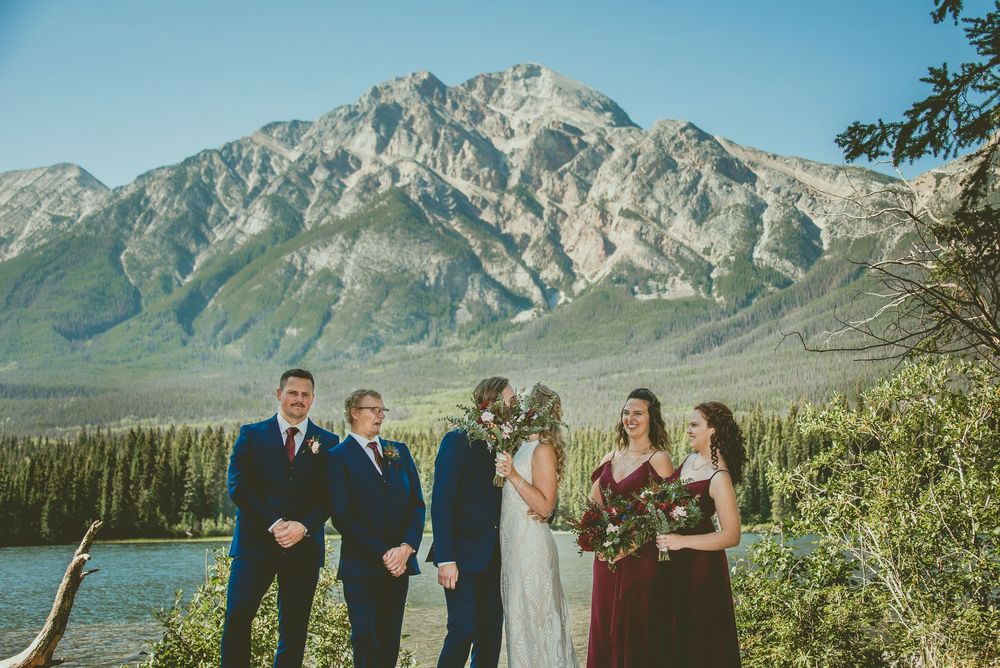 Micro Wedding party poses before stunning mountain lake backdrop in Banff, bride and groom flanked by groomsmen and bridesmaid.