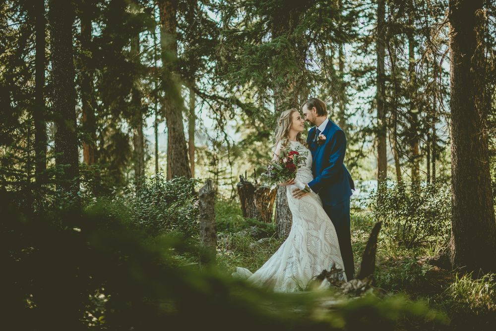 Bride and groom share romantic moment surrounded by tall trees in a sunlit forest wedding photo.
