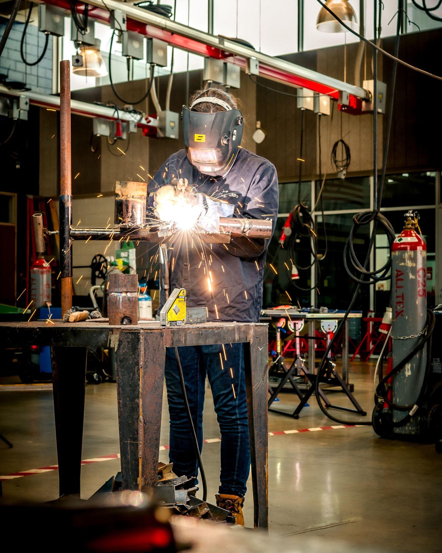 A welder in protective gear creates bright sparks while working on metal in an industrial workshop.