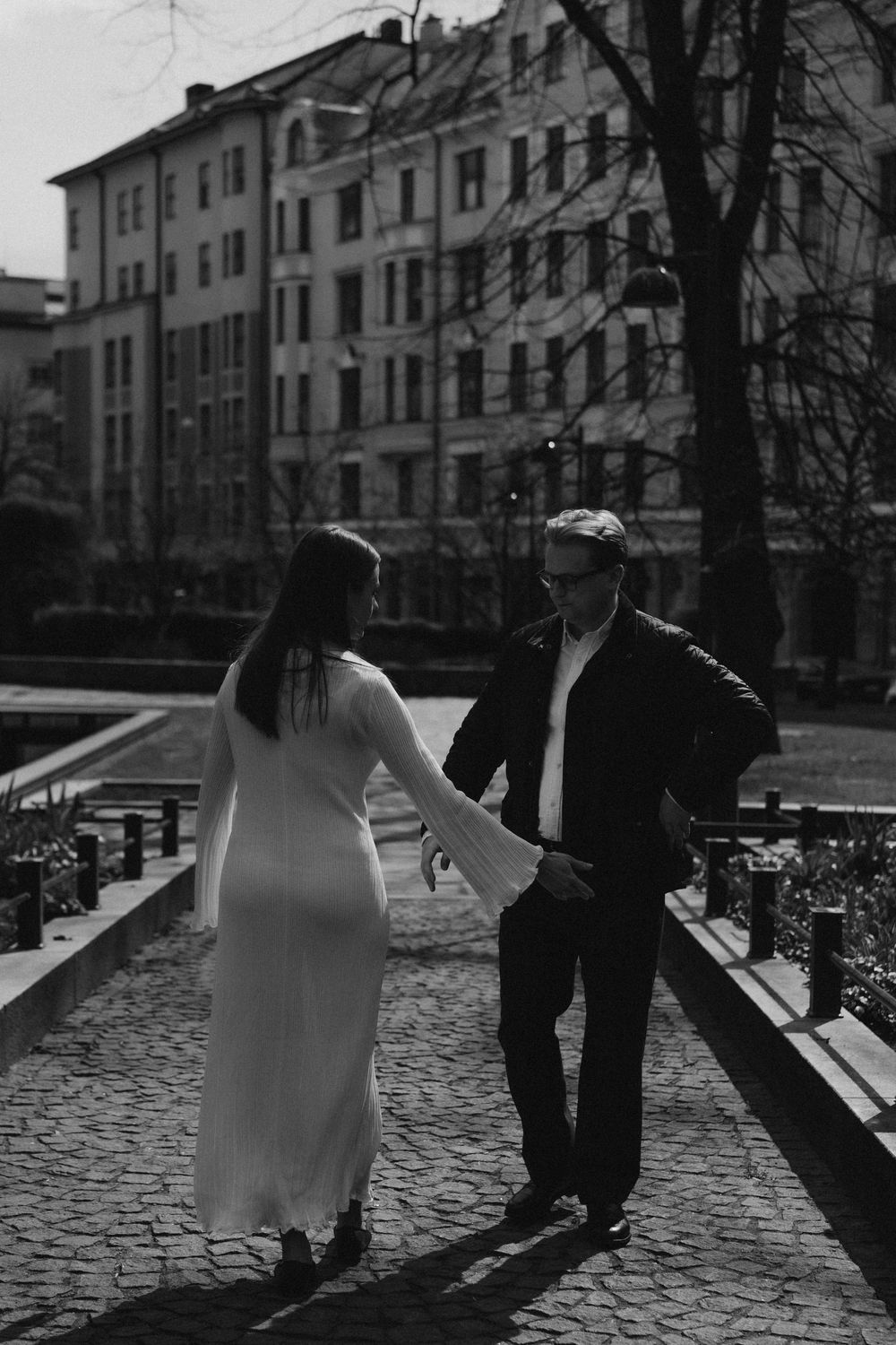Black and white engagement photo of a couple walking hand in hand by the water in Helsinki city centre