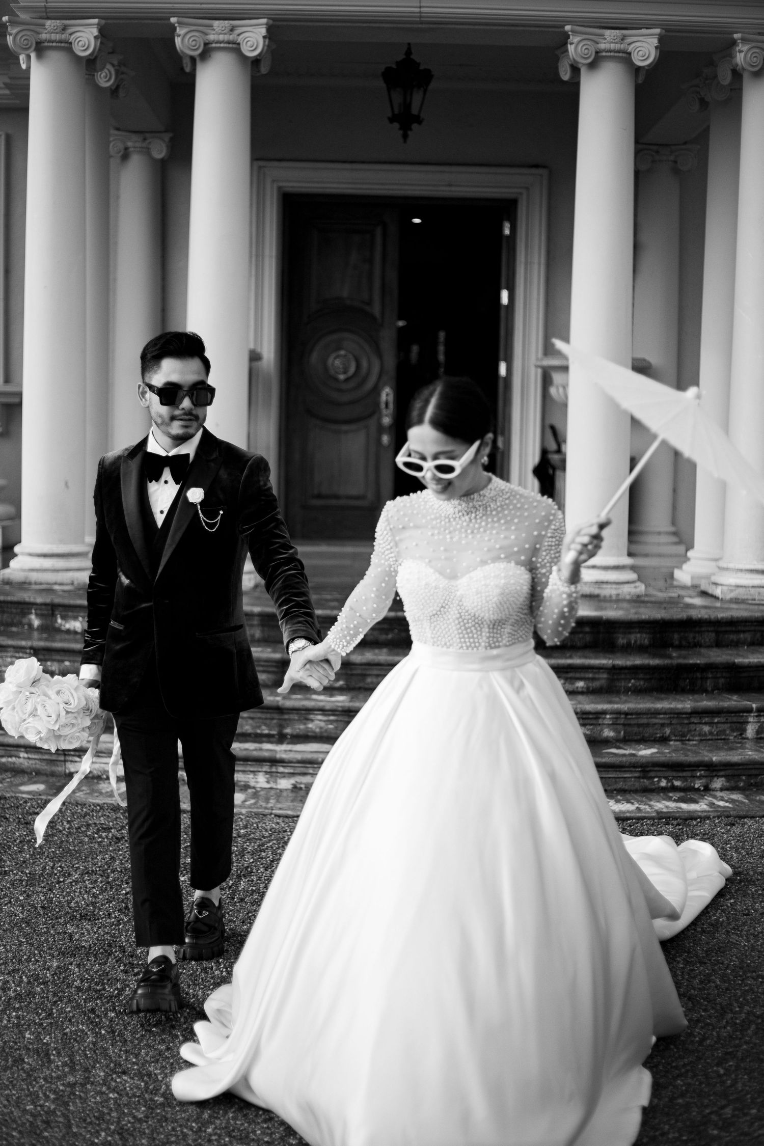 A playful wedding couple wearing sunglasses poses in front of a classic columned building entrance.