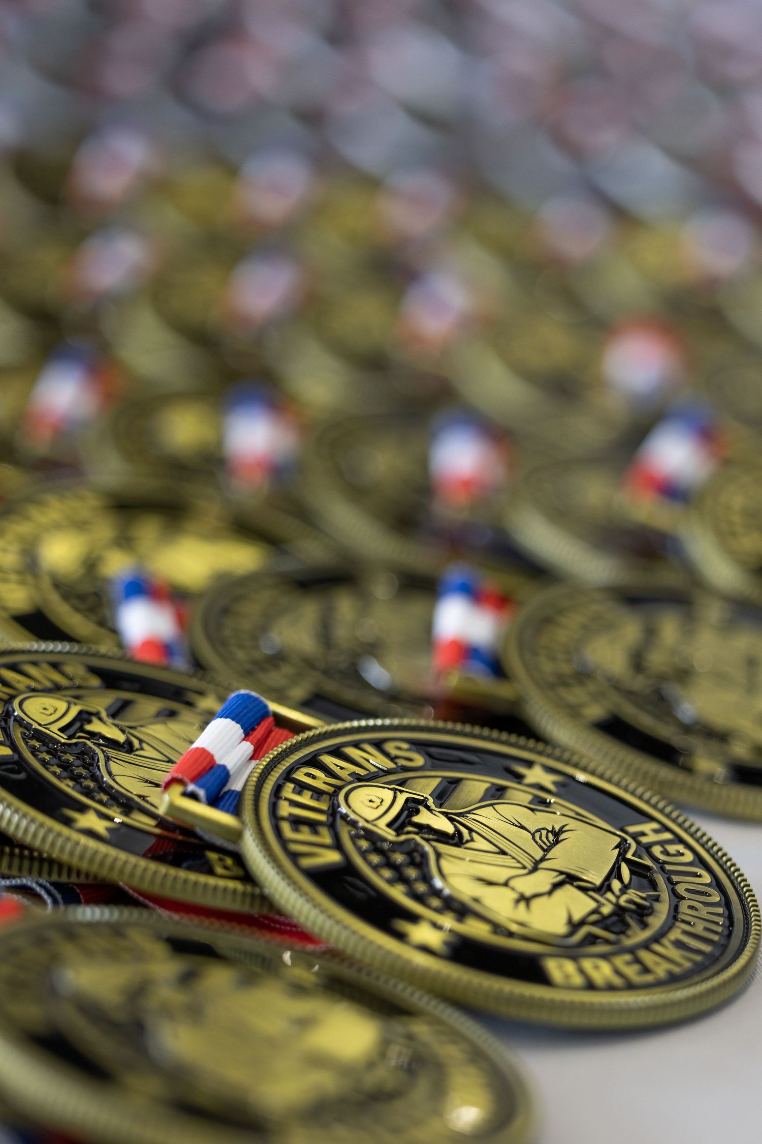 Rows of gold Veterans Breakthrough medals with red, white, and blue ribbons arranged on a flat surface.