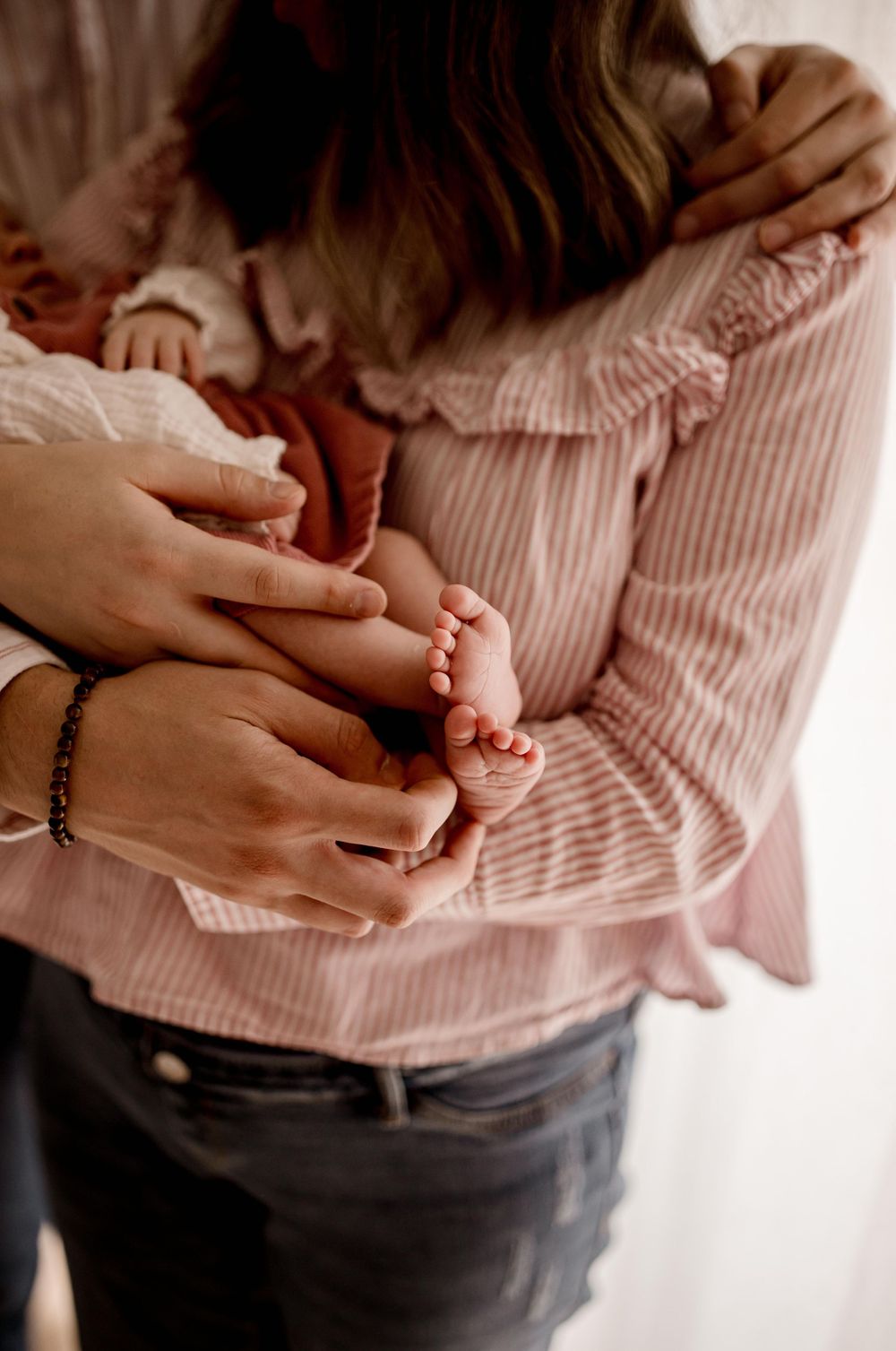 Gros plan de petits pieds de bébé tenus par des mains douces contre un tissu rayé rose.