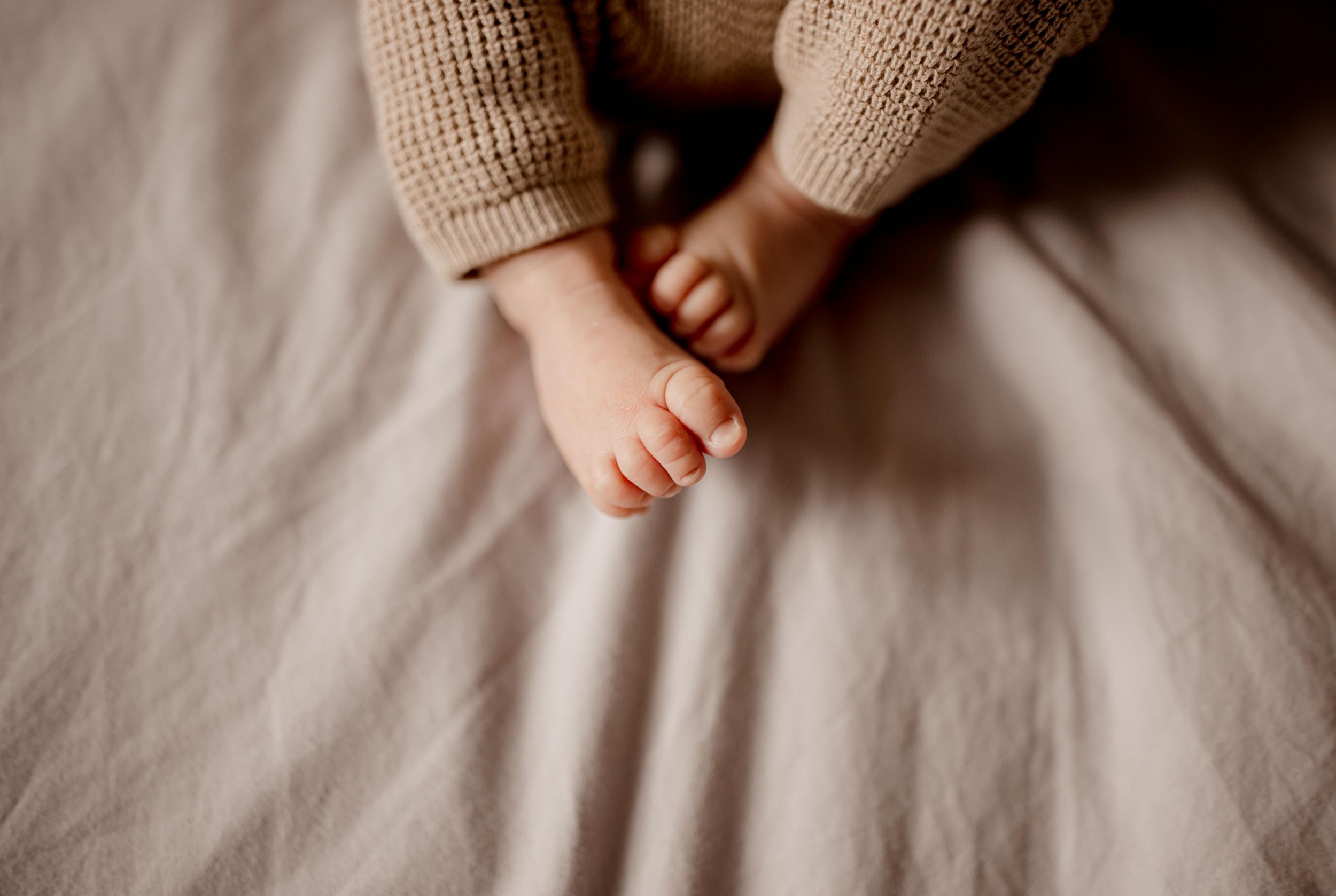 Gros plan de petits pieds de bébé sur un tissu en tricot beige doux.