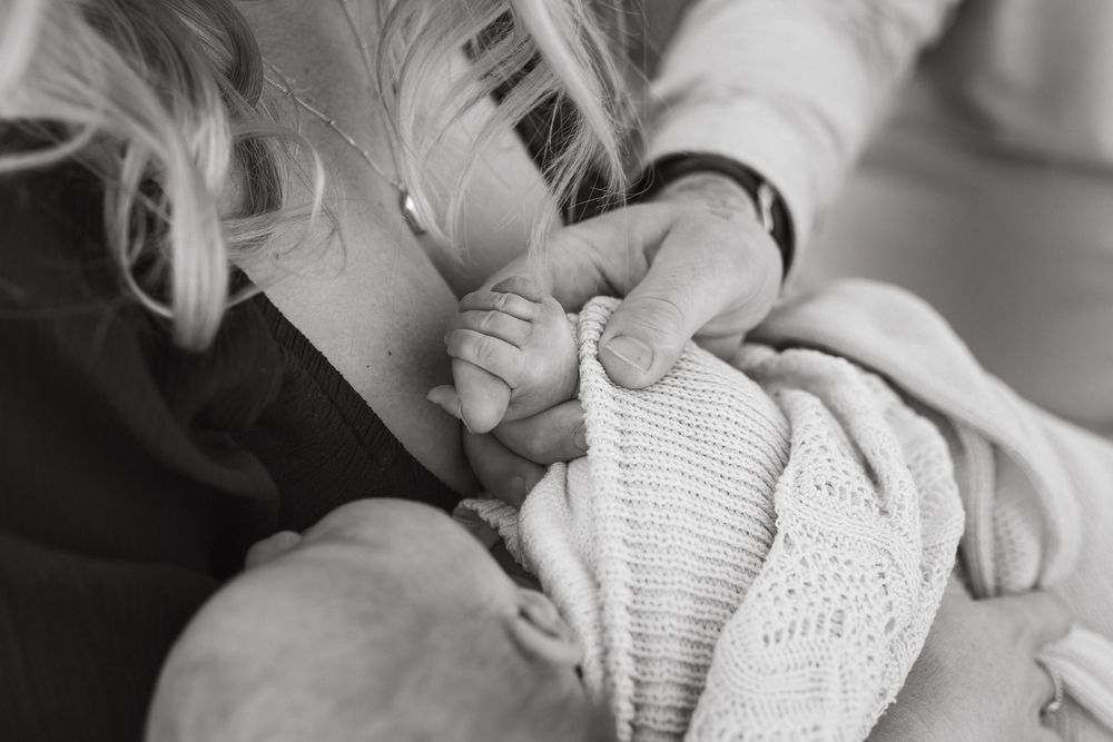 Black and white photo of a young child holding a newborn baby's tiny hand wrapped in a soft knit blanket.