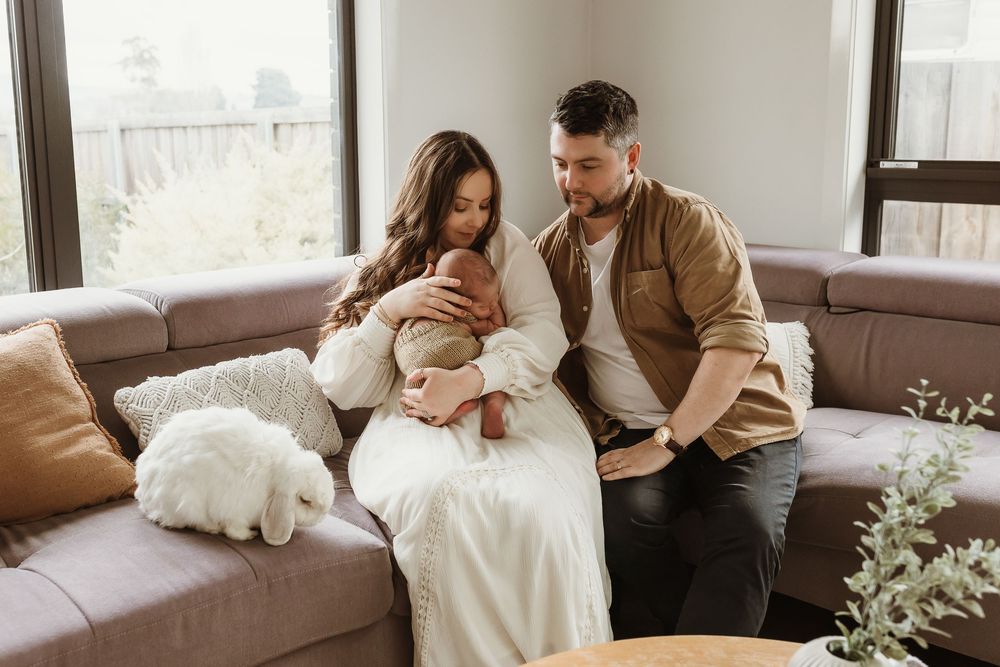 Young couple sitting on a couch admiring their newborn baby in a bright modern living room.