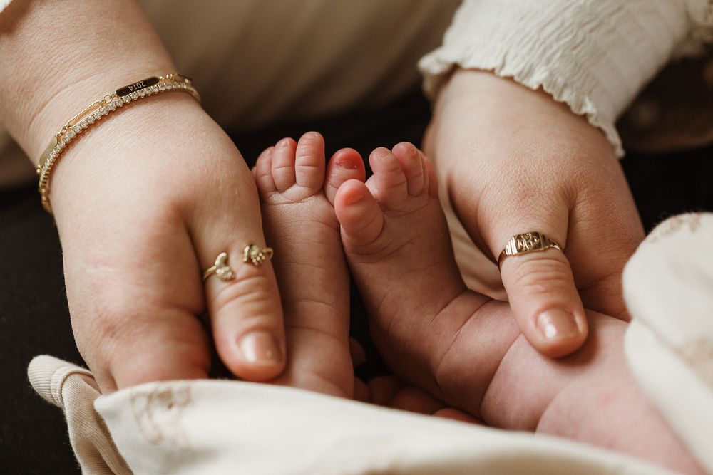 Two adult hands cradling tiny newborn baby feet, with gold rings visible on fingers.