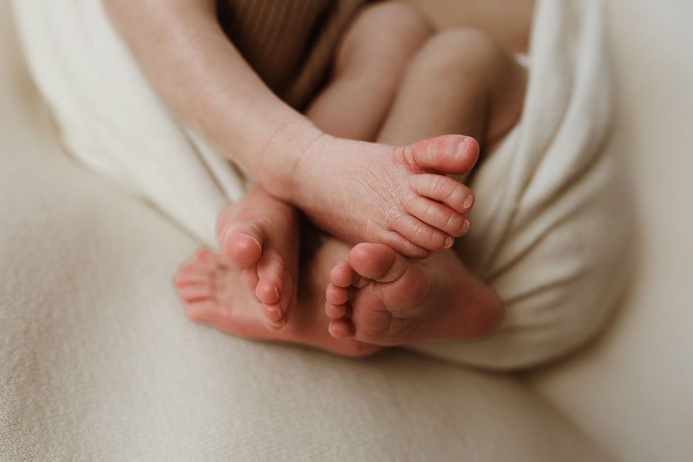 Close-up of newborn baby tiny feet and toes wrapped in a soft cream blanket.
