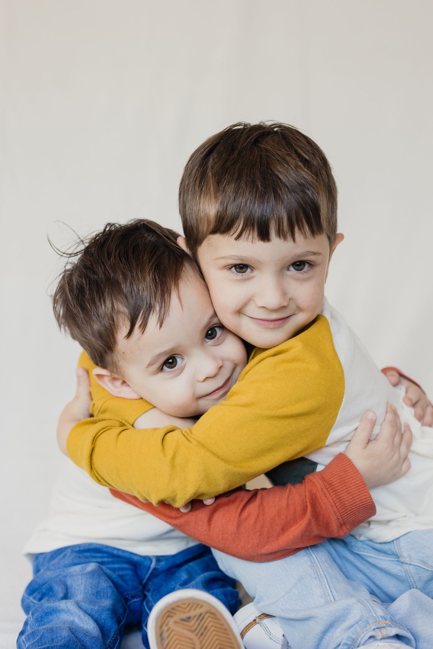 Two children in colorful sweaters sharing warm embrace against white background.