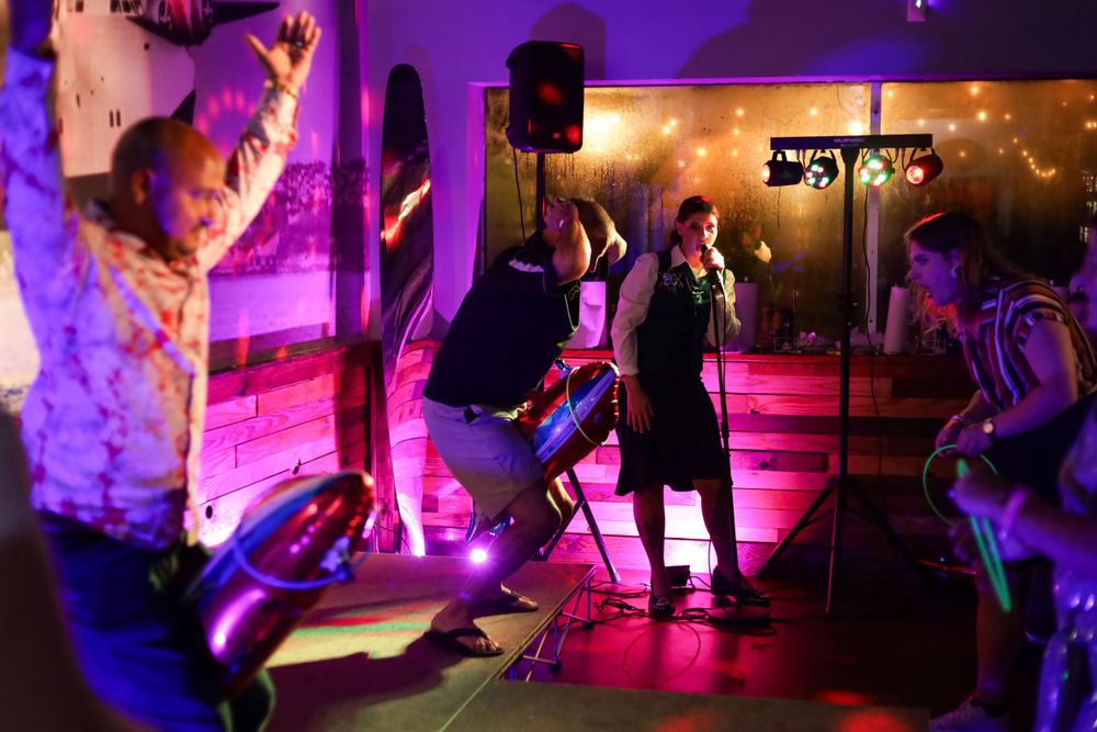 Live band performance with musicians and dancers under vibrant purple and pink stage lighting.
