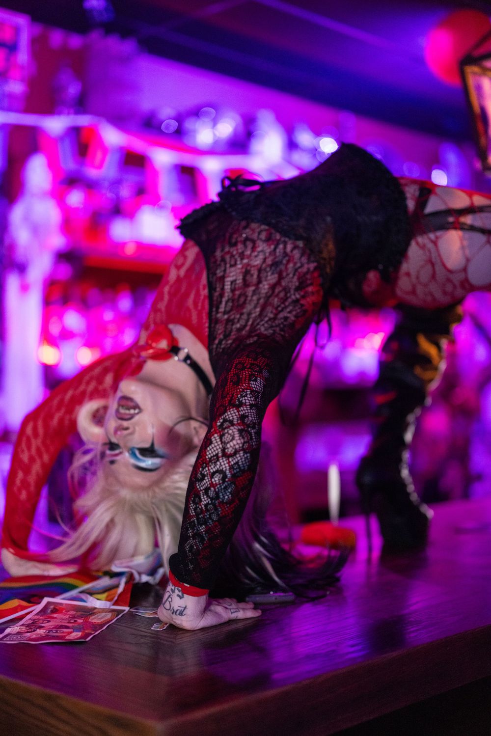 Person in Harley Quinn costume posing on a bar counter in a vibrant purple-lit nightclub setting.