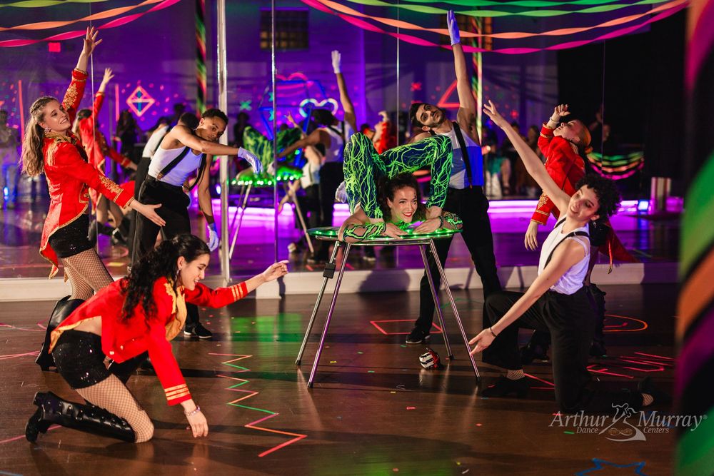 Energetic dance performance with red and green costumes under colorful lights at Arthur Murray event.