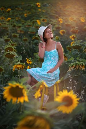 Candid moment in a sunflower field with someone in a blue dress sitting on a yellow chair.