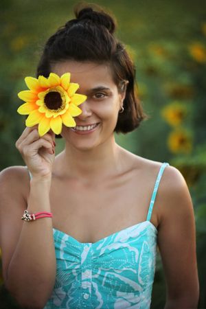 Summer portrait in a sunflower field with someone in a turquoise dress holding a bright yellow bloom.