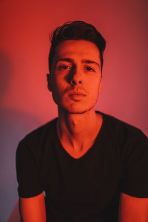 Portrait with dramatic red lighting and shadows against dark background.