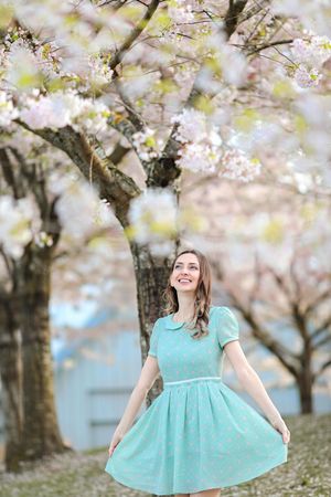 Spring portrait under blooming cherry trees with a turquoise vintage-style dress against soft pink blossoms.