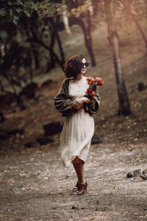 A whimsical forest scene with someone wearing a flowing dress while holding orange flowers.