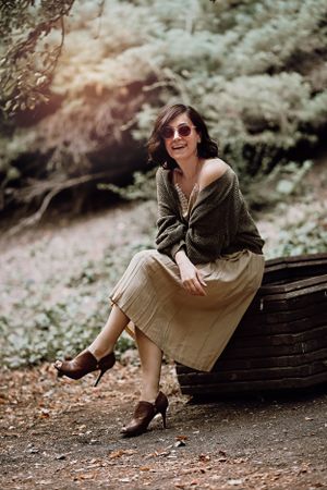 A casual outdoor portrait with someone wearing sunglasses and a cozy sweater while sitting on wood logs.