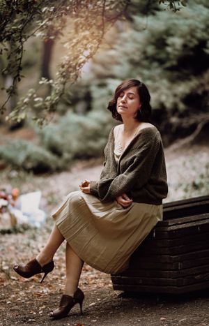 Vintage-style autumn portrait of woman in cardigan sitting on wooden bench.