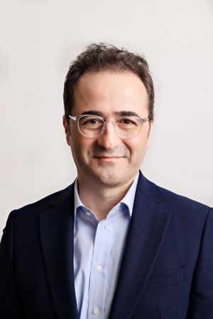 Corporate portrait of a professional in glasses and navy suit against white backdrop.