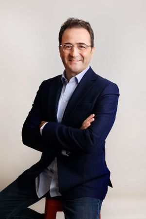 Professional headshot of a businessman in a navy blazer and light blue shirt against white background.