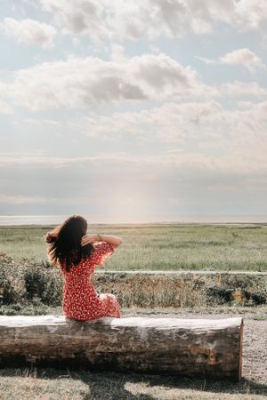 Person in a red floral dress sits on a stone wall overlooking a vast prairie landscape.