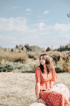 Person in a red floral dress sitting on a rock in a serene natural setting.