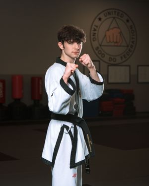 Martial artist performs a fighting stance in traditional white taekwondo uniform with black belt in a training studio.