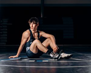 Athlete in dark workout gear sits on wrestling mat during training session.