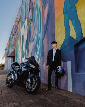 A sleek black motorcycle parked against a vibrant colorful mural wall with a person standing in formal attire.