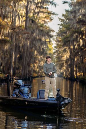 A fishing boat glides through cypress swamp waters draped with Spanish moss in golden afternoon light.