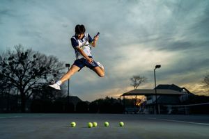 A tennis player serves the ball during sunset on an outdoor court as shown in a dynamic action sequence.