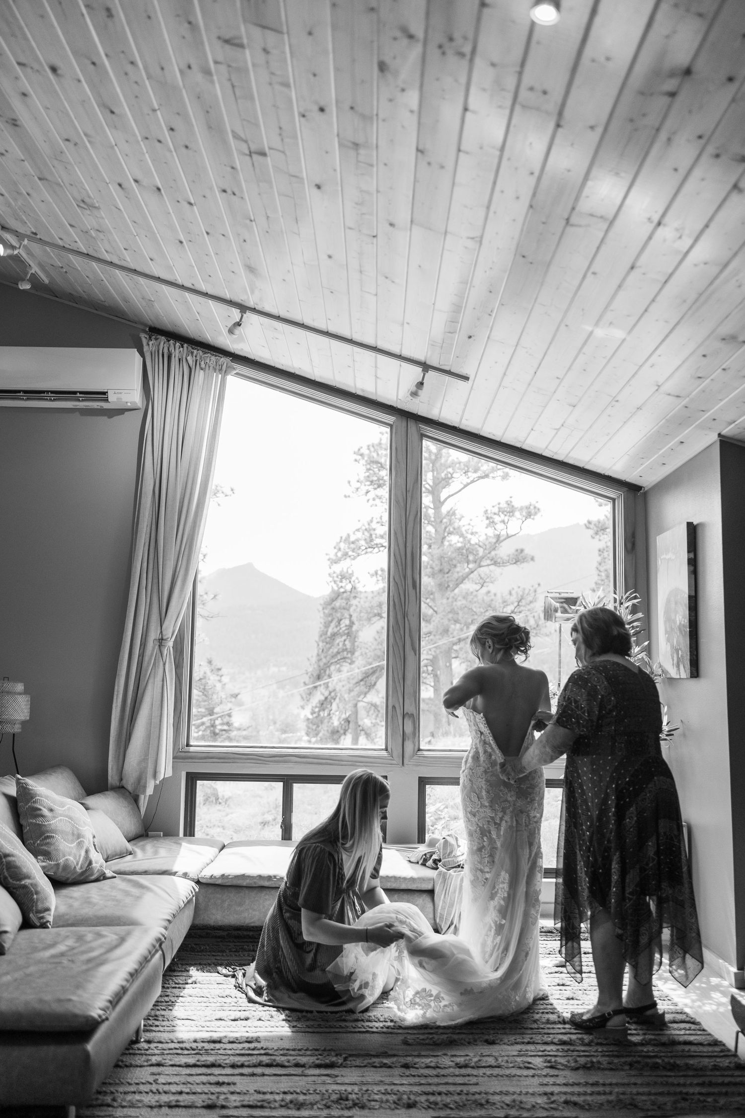 A black and white photo of wedding preparations in a modern mountain cabin with large windows and wooden ceiling.